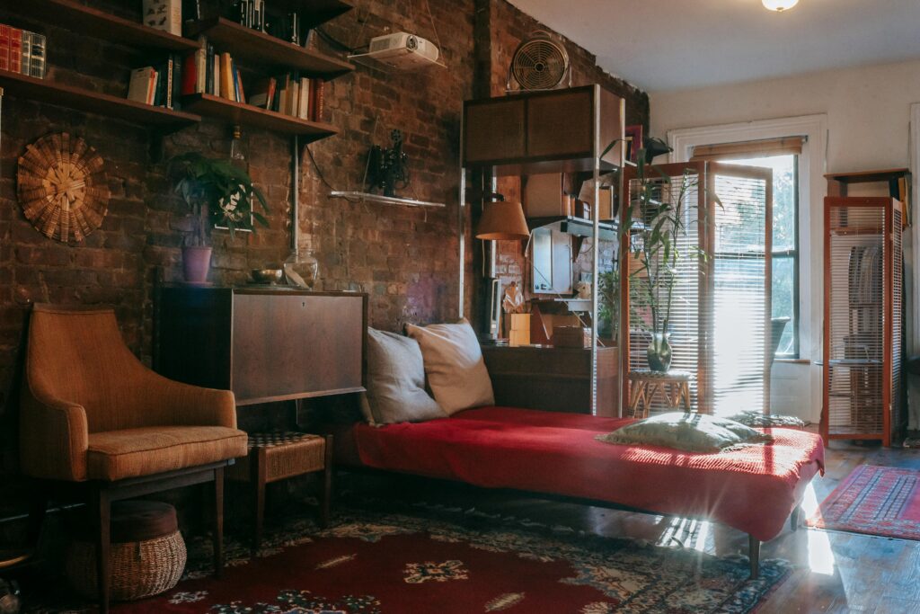 Vintage styled bedroom interior with classic wooden furniture and bookshelves decorated weathered brick wall near comfortable bed and armchair