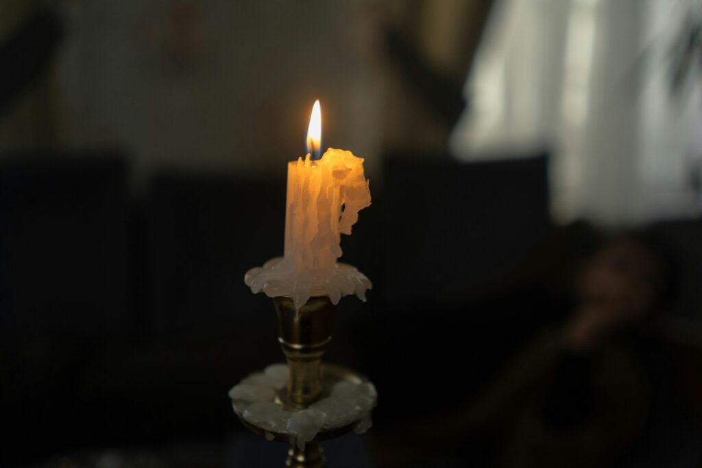 A burning candle with a dramatic wax drape brings a moody ambiance to a dimly lit room.