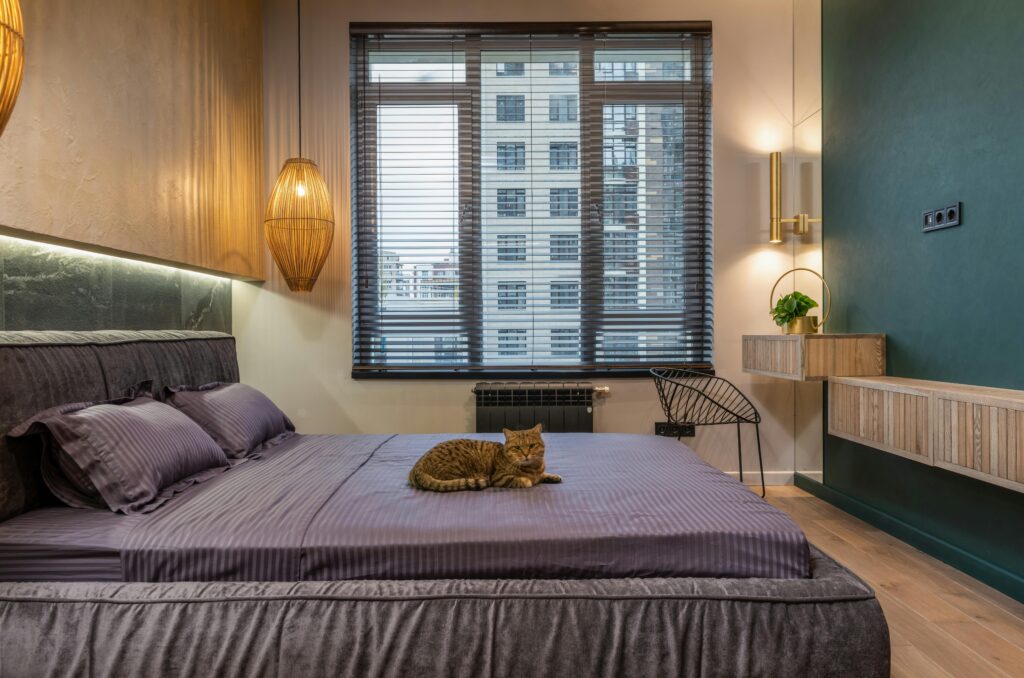 Luxurious modern bedroom interior with a relaxed cat, soft lighting, and urban view.