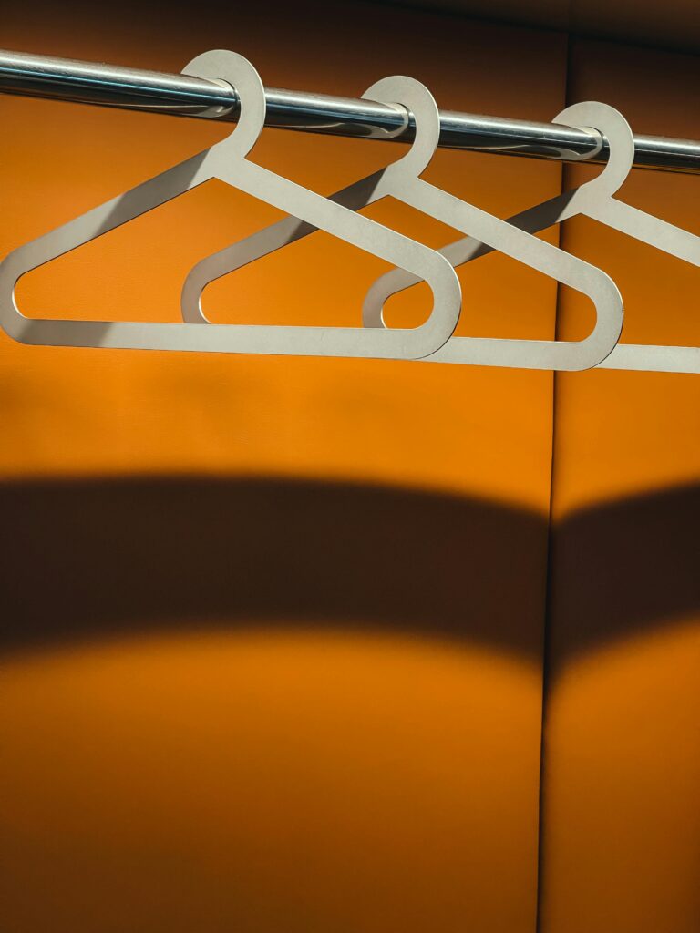 Three wooden hangers hanging on a metal rod against a bright orange wall. Minimalist design.