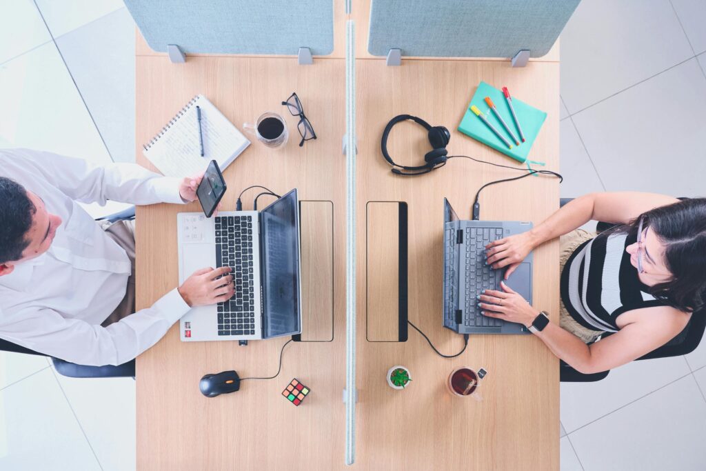 Two professionals working at a shared office desk, top view.